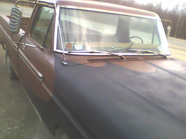 Brown 1970s Ford pickup truck with a matte black hood, seen from the front three-quarter angle
