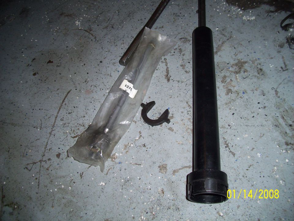 Car parts, including a shock absorber and a tie rod in plastic, lie on a concrete floor