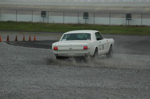 2007 Ford Mustang - A white first-generation Ford Mustang notchback coupe running an autocross course, caught from behind spraying gravel as it slides off the…