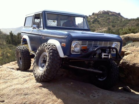 1988 Ford Bronco - First-gen Ford Bronco navigating a rocky trail with its suspension articulated.