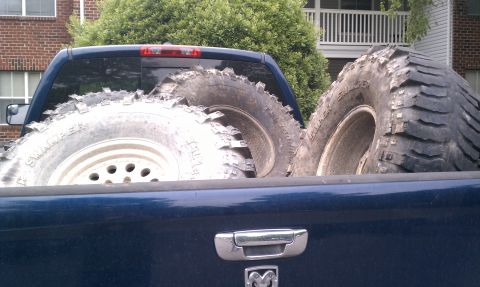 1990 Ford Bronco - Two large, knobby off-road tires are being transported in the bed of a dark blue pickup truck.