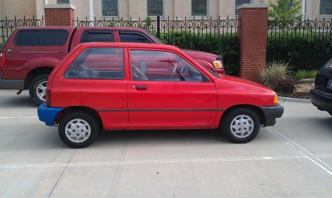 1991 Ford Festiva - A red 1991 Ford Festiva is parked next to a red pickup truck.