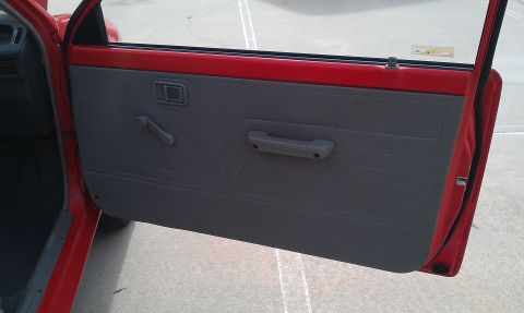 1991 Ford Festiva - Interior view of a red car door with a gray panel, manual window crank, and door handle.