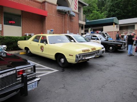 1991 Ford LTD Crown Victoria - yellow State Police sedan parked among other vintage police cars outside a brick building with people standing nearby.