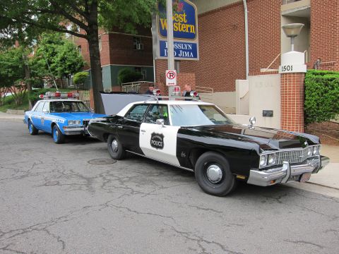 1991 Ford LTD Crown Victoria - black-and-white Chevrolet Police sedan and a blue police car parked on a street in front of a Best Western hotel.