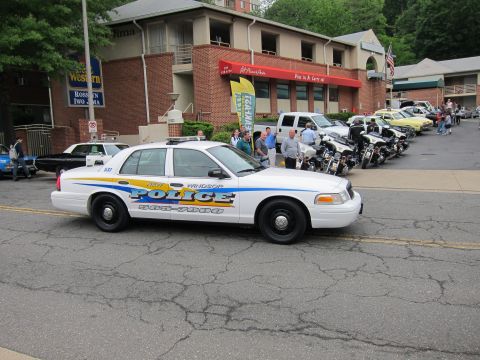 1991 Ford LTD Crown Victoria - white New Windsor Police sedan with blue and yellow markings parked near a brick building and a row of motorcycles.