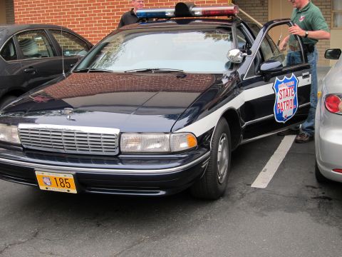 1991 Ford LTD Crown Victoria - Front three-quarter view of a dark blue Chevrolet Caprice State Patrol car with a roof light bar and yellow license plate.
