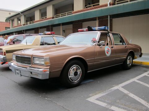 1991 Ford LTD Crown Victoria - brown Chevrolet Caprice police sedan with a roof light bar and circular door emblem parked at an angle.
