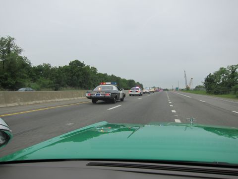 1991 Ford LTD Crown Victoria - Dashboard view from a green car of a black State Patrol cruiser and other police cars driving down a multi-lane highway.
