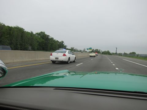 1991 Ford LTD Crown Victoria - View over a green hood of a white police sedan and other cars driving along a divided highway under a gray sky.