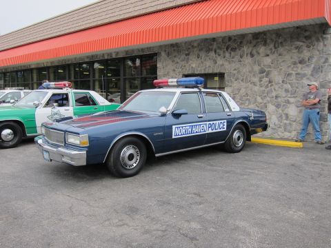 1991 Ford LTD Crown Victoria - dark blue Chevrolet Caprice marked North Haven Police with a roof light bar parked outside a stone-faced building.