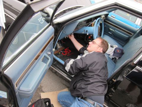 1991 Ford LTD Crown Victoria - man in a striped jacket lies across the open doorway reaching under the steering column of a car with blue bench seats.