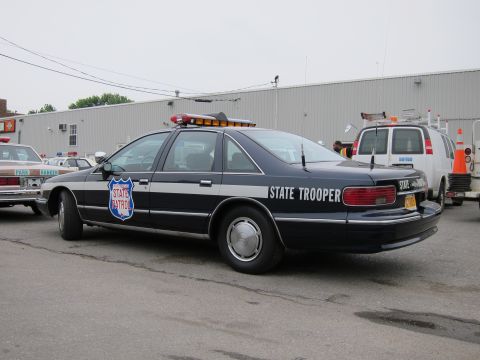 1991 Ford LTD Crown Victoria - Rear view of a black and silver Chevrolet Caprice marked State Trooper with a roof light bar, parked near a white van.