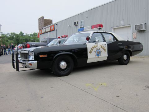 1991 Ford LTD Crown Victoria - black-and-white California Highway Patrol-style sedan with front push bar and roof light bar parked outside a metal building.