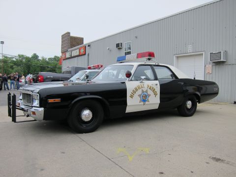 1991 Ford LTD Crown Victoria - black-and-white Highway Patrol sedan with a chrome front push bar and roof light bar, parked on pavement near a metal warehouse.