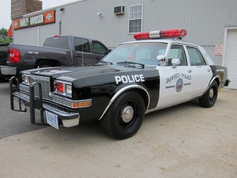 1991 Ford LTD Crown Victoria - black-and-white Jaffrey Police sedan with chrome push bar and roof light bar, parked near a Harley-Davidson storefront.