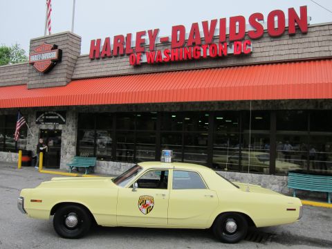 1991 Ford LTD Crown Victoria - yellow State Police sedan with door shield decal parked in profile in front of the Harley-Davidson of Washington DC storefront.