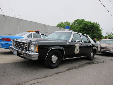 1991 Ford LTD Crown Victoria - black-and-white full-size police sedan marked 45 with a blue beacon and gold department shield sits in a paved lot beside other classic car…