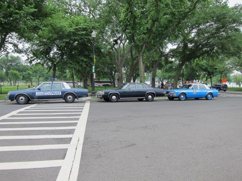1991 Ford LTD Crown Victoria - Three vintage police sedans, including a blue North Haven Police car, are parked on pavement among trees in a park.