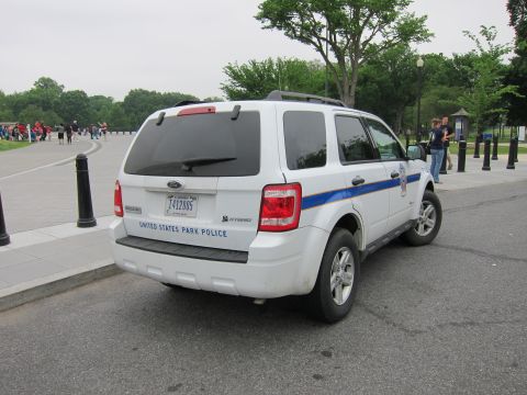 1991 Ford LTD Crown Victoria - white Ford Escape hybrid SUV marked United States Park Police with a blue stripe is parked on a paved path.