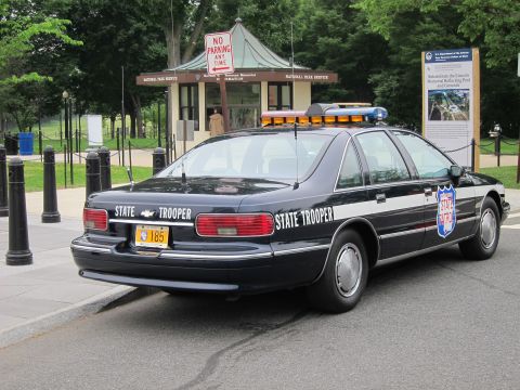 1991 Ford LTD Crown Victoria - dark State Trooper sedan with an amber roof light bar and shield decal sits near a National Park Service kiosk.