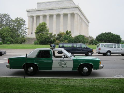 1991 Ford LTD Crown Victoria - green-and-white Sheriff patrol sedan sits in profile before the Lincoln Memorial, with vans parked behind it.