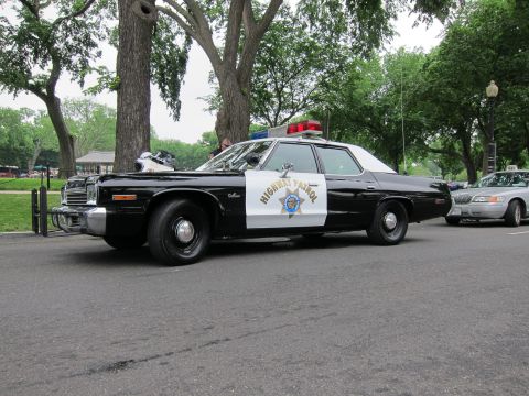 1991 Ford LTD Crown Victoria - black-and-white Highway Patrol sedan with a push bar and motorcycle nearby is parked along a tree-lined park street.