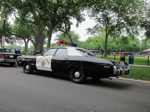 1991 Ford LTD Crown Victoria - black-and-white Highway Patrol sedan with a roof light bar and rear push bar is parked among trees in a park.