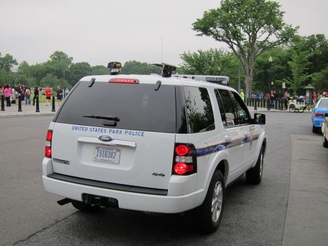 1991 Ford LTD Crown Victoria - Rear three-quarter view of a white Ford Explorer SUV marked United States Park Police with a roof light bar, parked among a crowd of pedest…