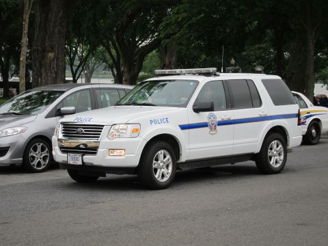 1991 Ford LTD Crown Victoria - Front three-quarter view of a white Ford Explorer police SUV with POLICE lettering, blue stripe and a circular agency emblem, parked among…