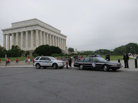 1991 Ford LTD Crown Victoria - white police SUV and a black and white police sedan parked on the plaza in front of the Lincoln Memorial as visitors gather nearby.
