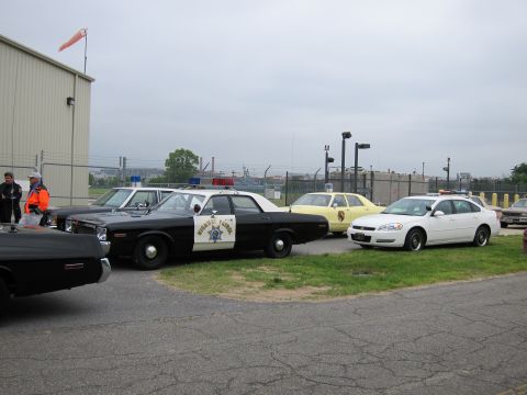 1991 Ford LTD Crown Victoria - black-and-white California Highway Patrol cruiser parked beside a white modern police sedan and other cars in a paved lot near a chain-link…