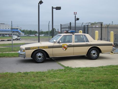 1991 Ford LTD Crown Victoria - Side view of a tan and brown STATE POLICE Chevrolet Caprice sedan with a Maryland shield emblem and roof light bar, parked on a concrete pa…