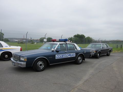 1991 Ford LTD Crown Victoria - dark blue Chevrolet Caprice marked NORTH HAVEN POLICE with roof beacons parked beside an older sedan near a chain-link fence.