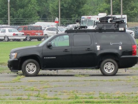 1991 Ford LTD Crown Victoria - black Chevrolet Suburban with roof-mounted tactical gear parked in a lot, viewed from the front three-quarter angle.