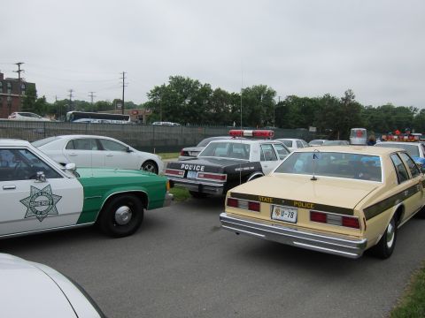 1991 Ford LTD Crown Victoria - Several vintage police cars are parked together, including a green and white sheriff sedan and a tan state police sedan.