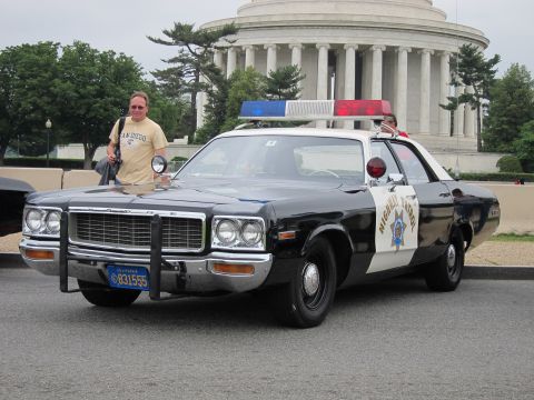 1991 Ford LTD Crown Victoria - man in a yellow shirt stands beside a black and white California Highway Patrol sedan before a columned domed memorial.