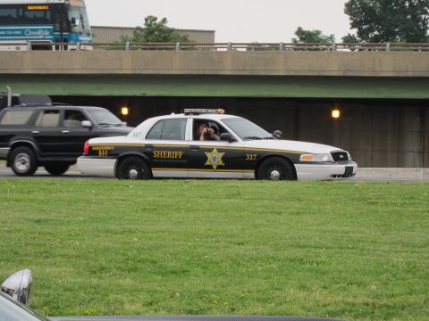 1991 Ford LTD Crown Victoria - black and white Ford Crown Victoria sheriff cruiser marked 317 drives beneath a highway overpass past a bus.