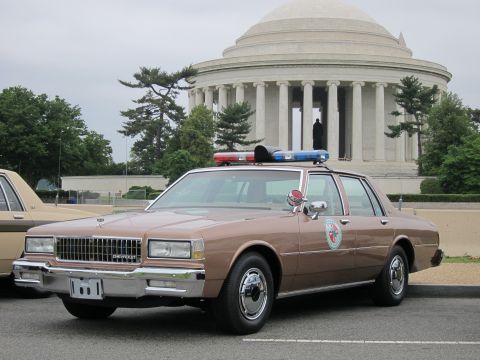 1991 Ford LTD Crown Victoria - brown Chevrolet Caprice police sedan with a roof light bar is parked in front of the columned Jefferson Memorial.
