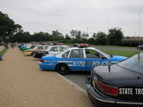 1991 Ford LTD Crown Victoria - blue NYPD Chevrolet Caprice and a State Trooper car among a row of police cruisers parked along a path.
