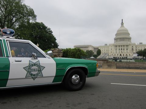 1991 Ford LTD Crown Victoria - Front of a green-and-white sheriff cruiser with California county star decal, the US Capitol dome in the background.