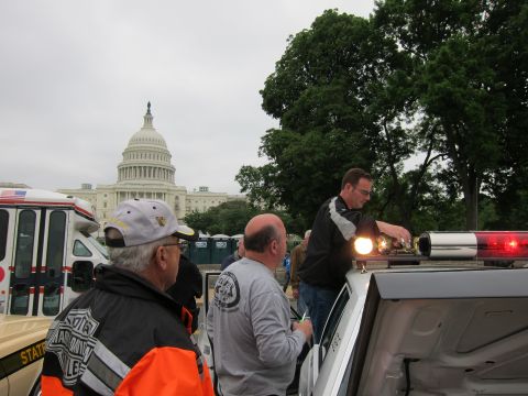 1991 Ford LTD Crown Victoria - Two men adjust the roof lights of a white police car near the US Capitol, another man in patrol jacket watching.