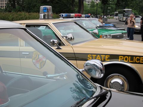 1991 Ford LTD Crown Victoria - Close-up of tan State Police sedans with chrome spotlight mirrors, roof lights, and a Maryland shield decal.