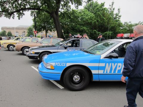1991 Ford LTD Crown Victoria - blue NYPD Chevrolet Caprice among parked police cars, a man in dark jacket walking past in the foreground.