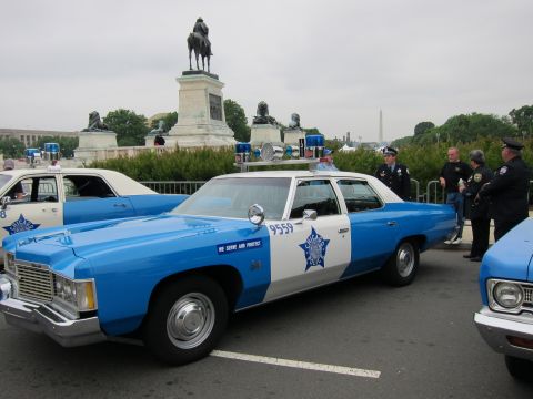 1991 Ford LTD Crown Victoria - blue and white vintage Chevrolet police sedan numbered 9559 with star emblem sits parked beside other cruisers near a DC equestrian statue…