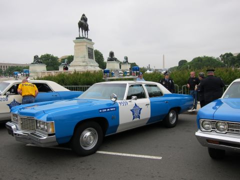 1991 Ford LTD Crown Victoria - blue and white vintage police sedan marked 9559 sits between other classic cruisers near a DC equestrian monument, with officers standing a…