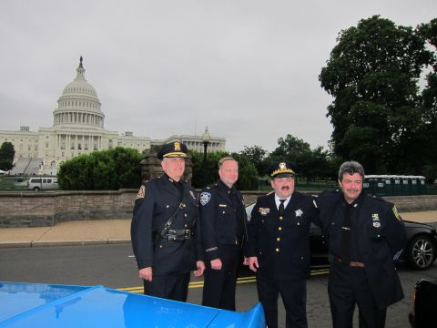 1991 Ford LTD Crown Victoria - Four uniformed police officers in dress blues pose together in front of the US Capitol building on an overcast day.