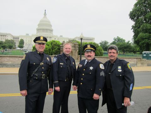 1991 Ford LTD Crown Victoria - Four police officers in dark dress uniforms with badges and caps pose in front of the US Capitol dome.