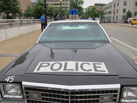1991 Ford LTD Crown Victoria - Close front view of a black vintage police car with 'POLICE' painted across the hood, number 45 on the fender, and a roof beacon.