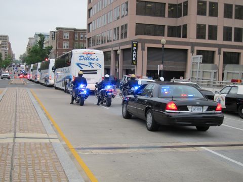 1991 Ford LTD Crown Victoria - black Ford police cruiser and two motorcycle officers lead an escort for a line of Dillon's tour buses along a downtown street.